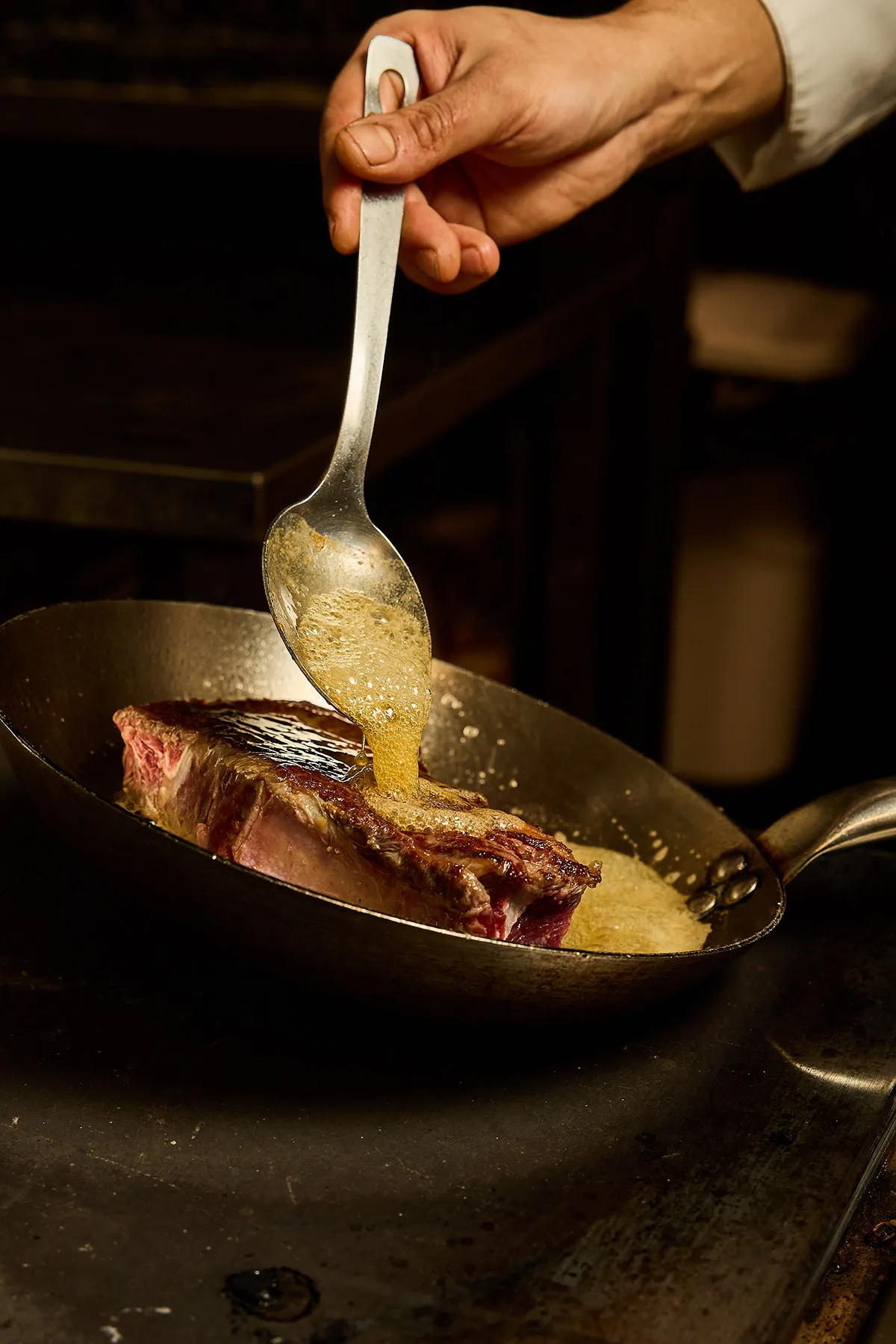 Chef arrosant un morceau de bœuf au beurre dans une poêle au restaurant italien In Casa à Levallois-Perret