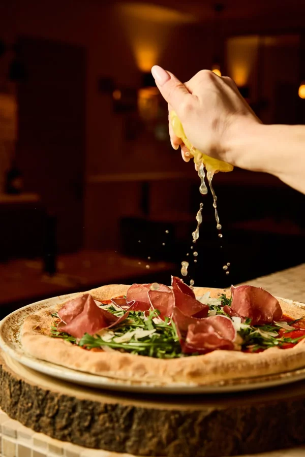 Pizza parma restaurant in casa levallois perret Main tenant un citron et qui assaisonne la pizza Parma servie dans le restaurant In Casa à Levallois-Perret