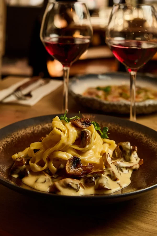 Tagliatelle crème de truffe, champignons, parmesan avec deux verres de vin rouge servi au restaurant in casa à levallois-perret