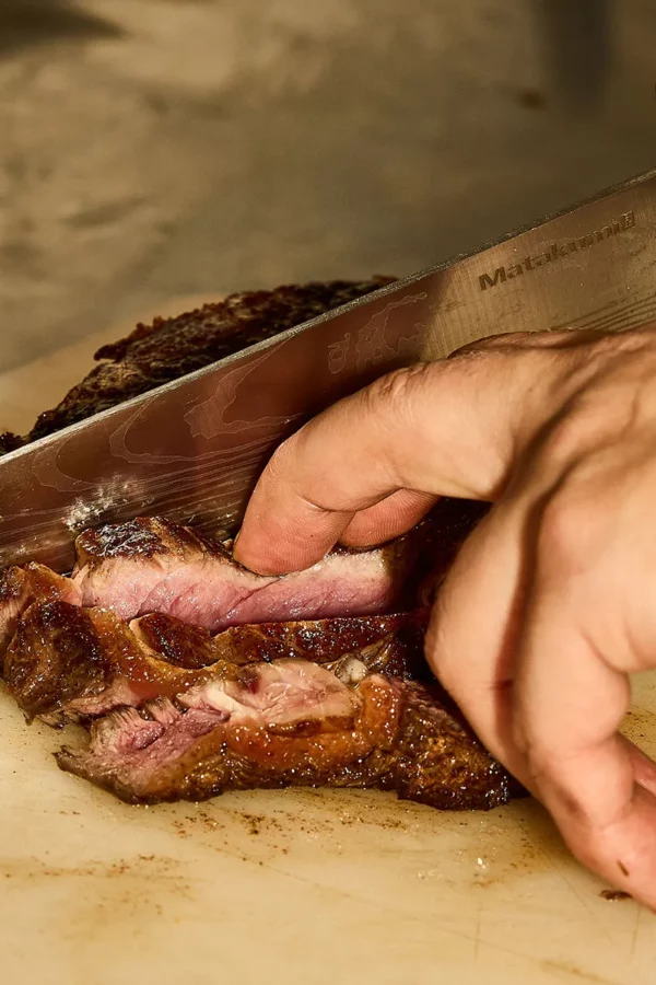 Chef découpant un morceau de bœuf saignant en cuisine au restaurant italien In Casa à Levallois-Perret
