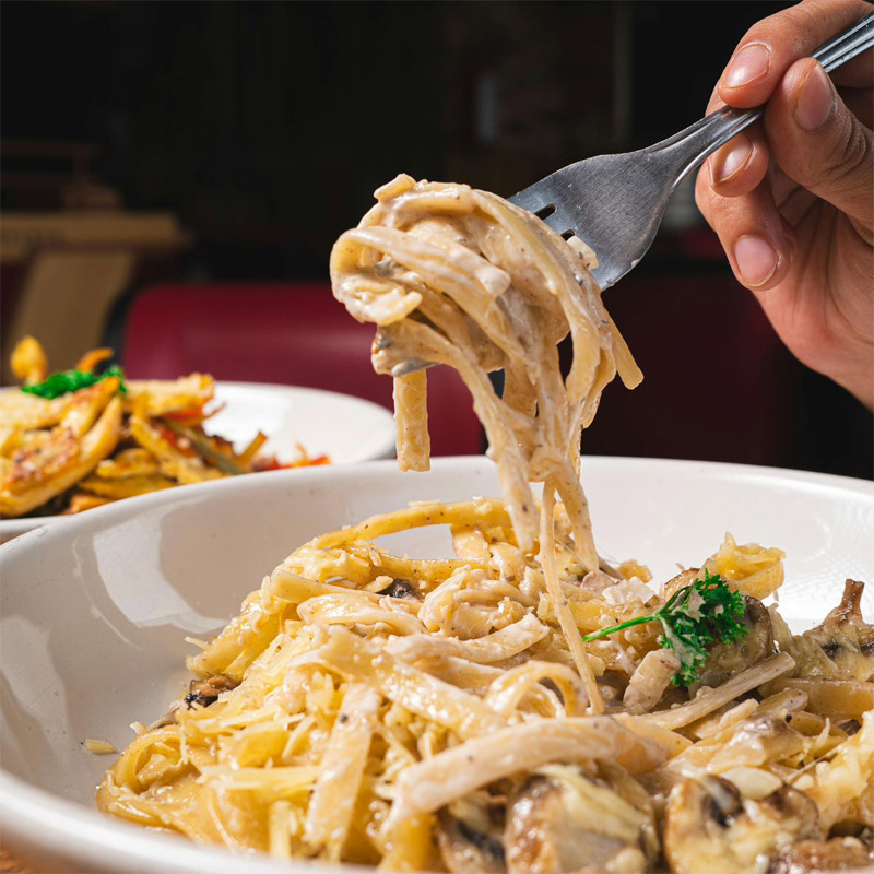 Linguine aux champignons et crème – In Casa Levallois Main tenant une fourchette avec des linguine aux champignons, crème et fromage, servies dans le restaurant In Casa à Levallois-Perret