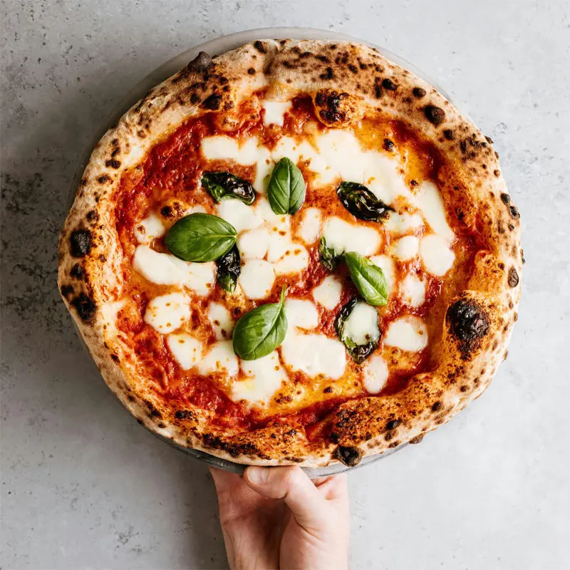 Pizza Margherita maison – In Casa Levallois Main tenant une pizza Margherita dans le restaurant italien In Casa à Levallois-Perret