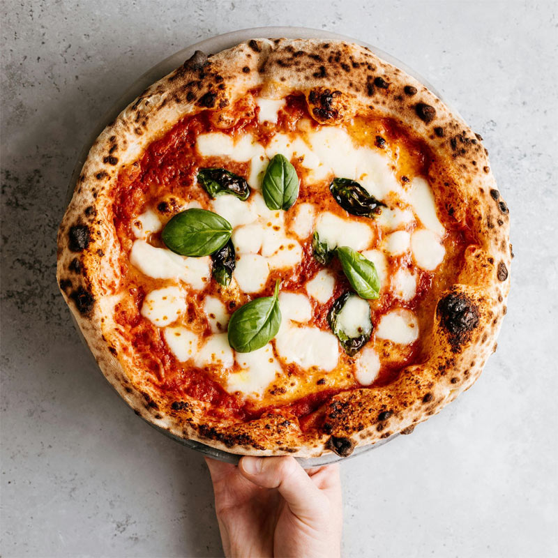 Pizza Margherita maison – In Casa Levallois Main tenant une pizza Margherita dans le restaurant italien In Casa à Levallois-Perret